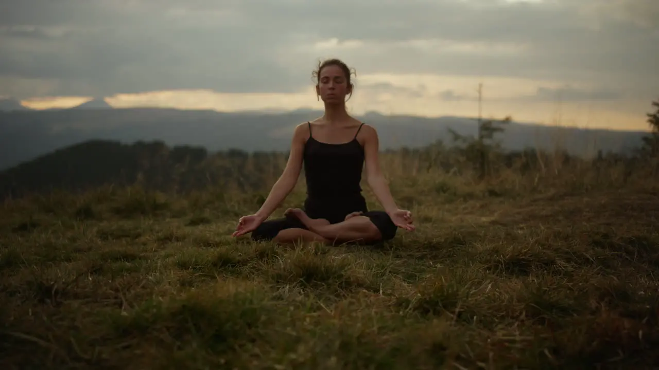 Serious woman sitting in lotus pose on grass Focused girl meditating outdoor