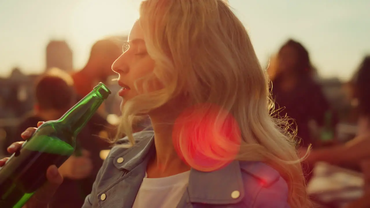 Young woman drinking beer at disco Smiling girl dancing at sunset roof party