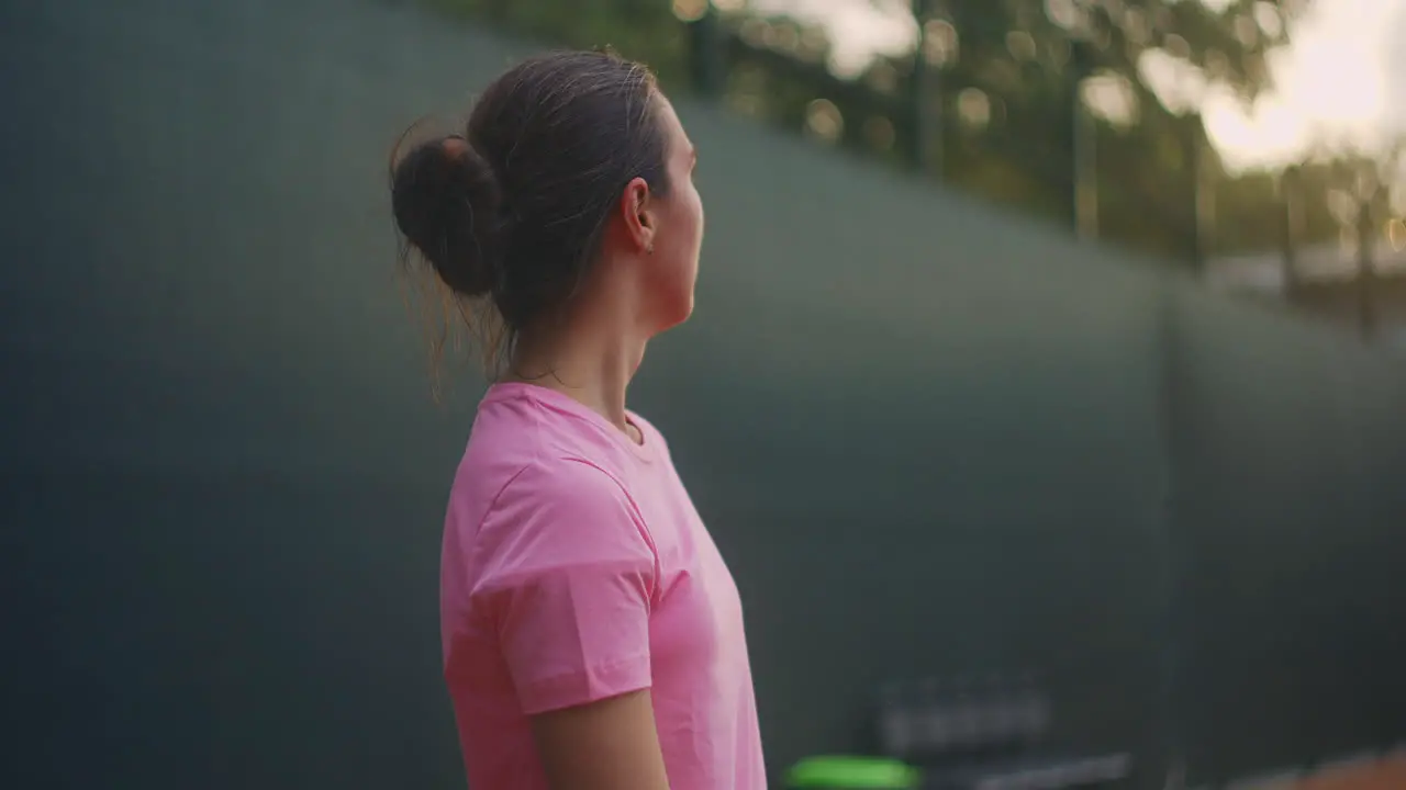 A female tennis player on the court at sunset after a match tired looking forward and concentrating after a hard game