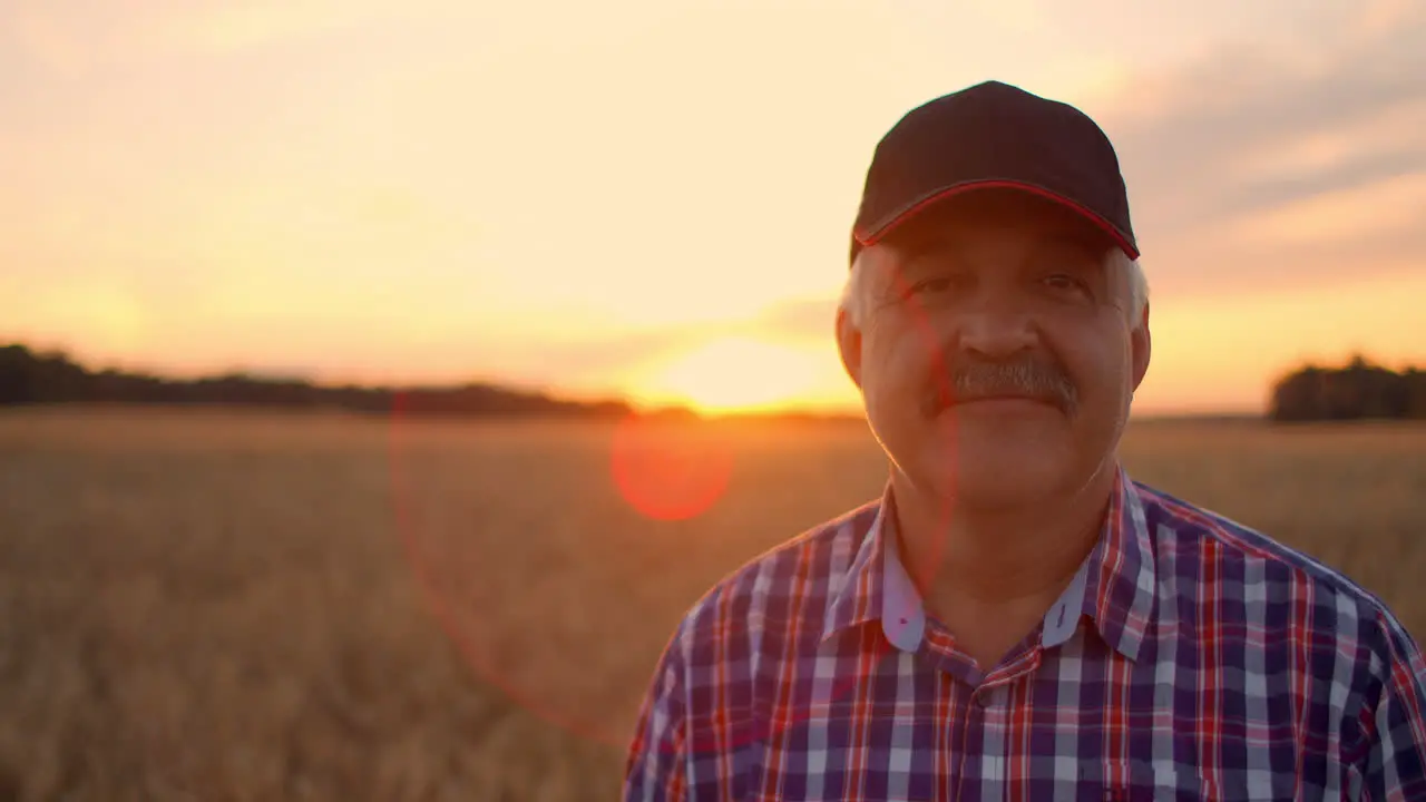 Portrait of a Senior adult farmer in a field of grain looking at the camera and smiling at sunset The tractor driver takes off his cap and looks at the camera in slow motion