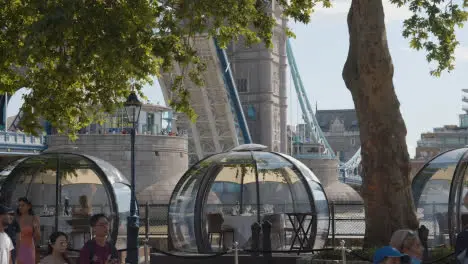 Crowd Of Summer Tourists Walking By Tower Bridge London England UK With Restaurant Pods In Foreground