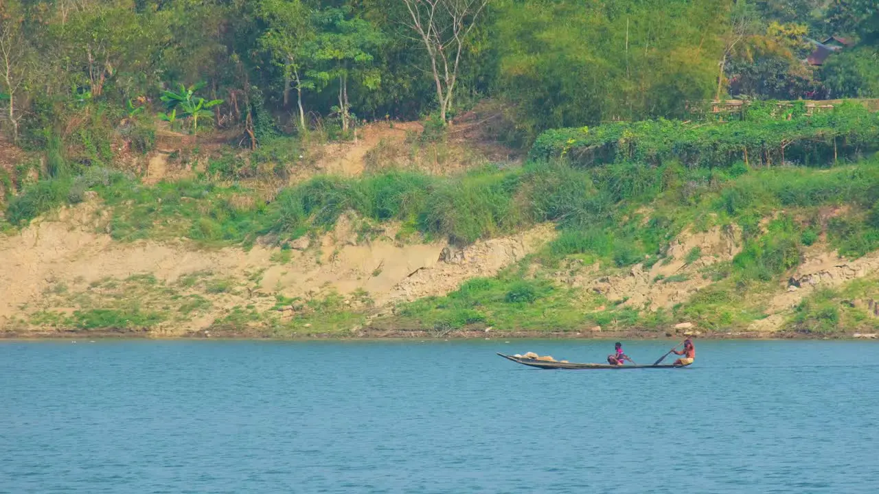 Two asian men row on a small traditional boat on river medium shot