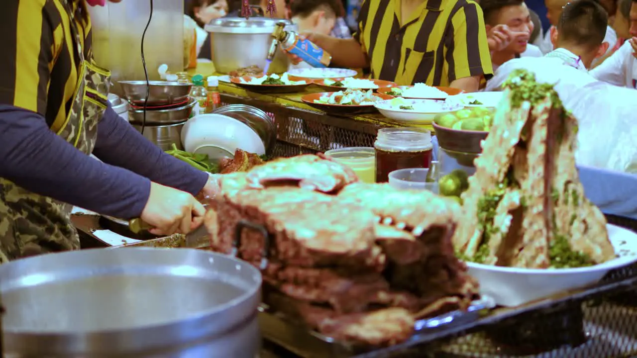 Black and Yellow uniform man cut meat on a busy night food market stall Bangkok