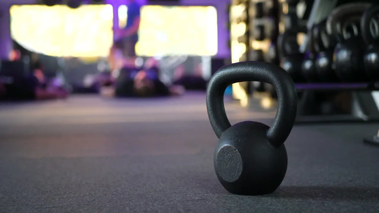 A kettlebell weight in a gym with people working out in a fitness training class in the background SLIDE RIGHT