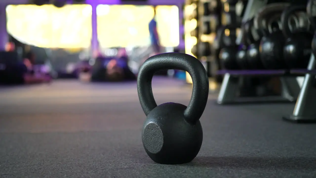 A kettlebell weight in a gym with people working out in a physical fitness training class in the background SLIDE LEFT