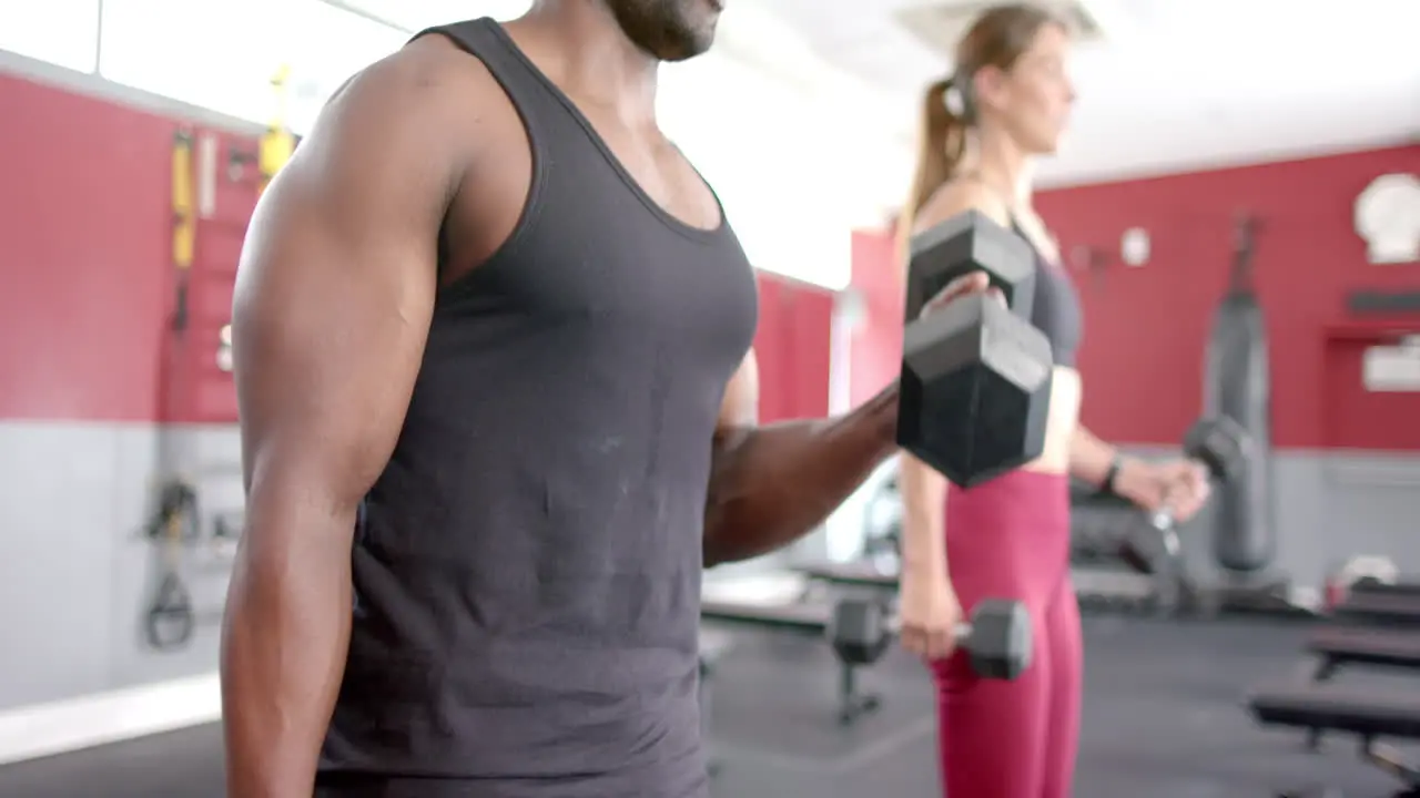 Fit African American man and young Caucasian woman exercising at the gym lifting weights