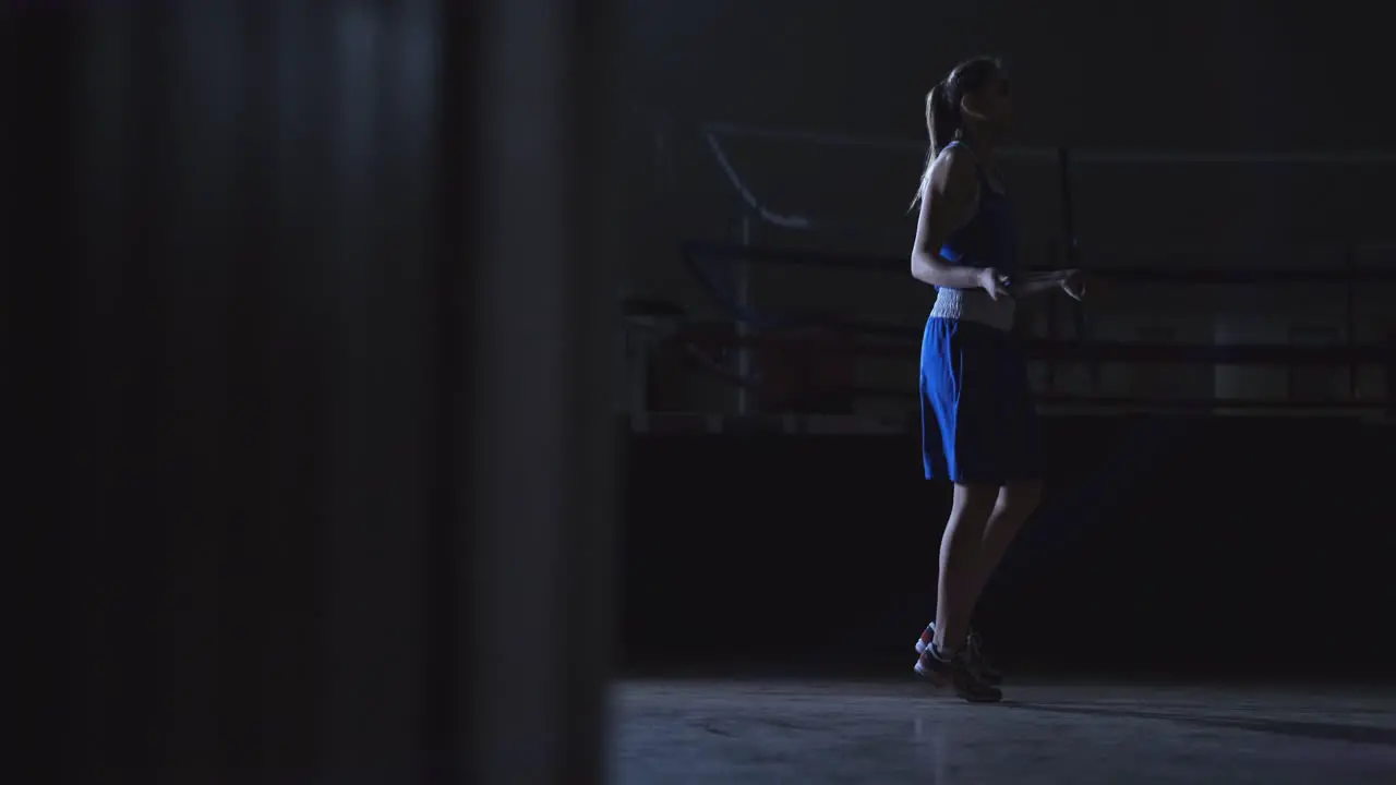 Cardio training for fighters Young beautiful woman professional boxer in training in the hall jumps on a rope in the light of the contra in a dark room in blue clothes