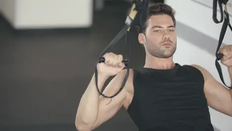 Athlete man using fitness loops for pull ups exercise in gym