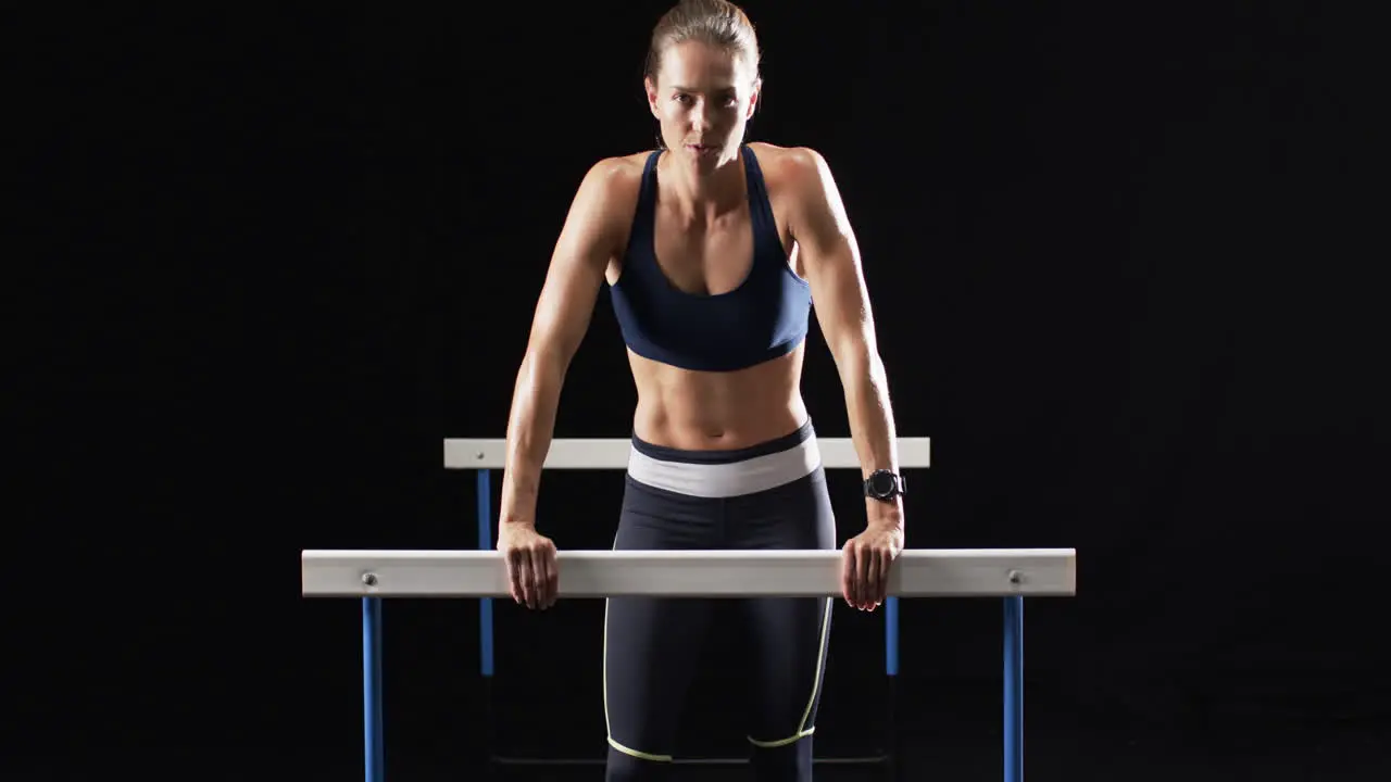 Young Caucasian woman performs a dip exercise on hurdles at the gym on a black background