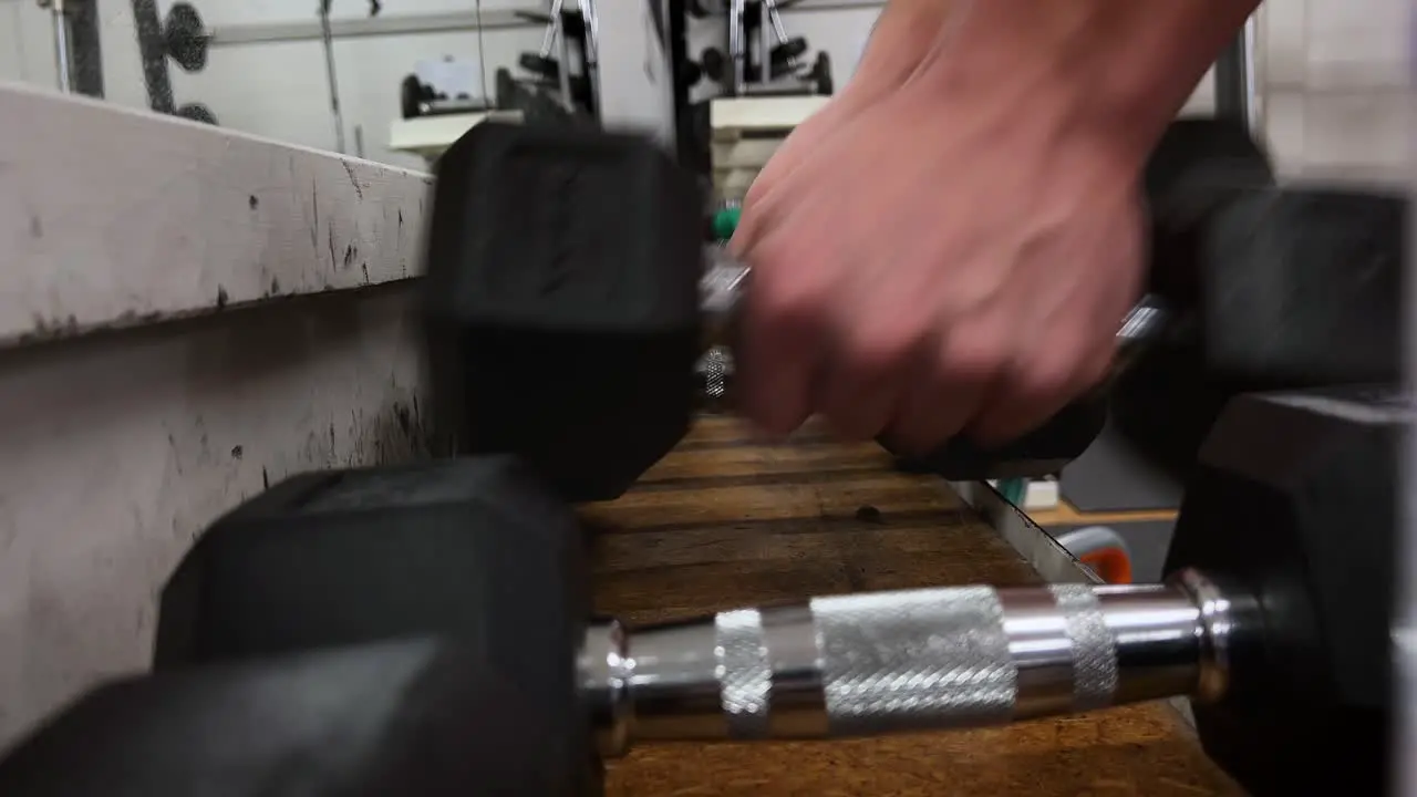 Male hands picking up dumbbell from gym bench