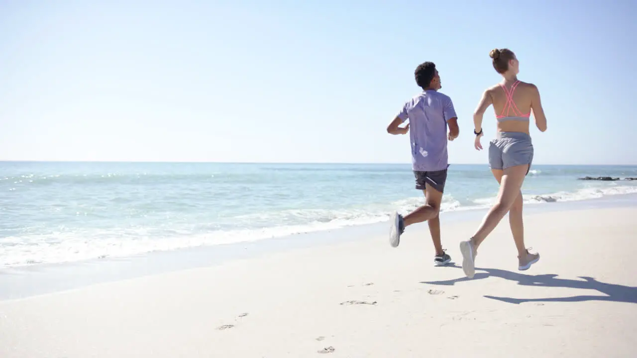 Young biracial man and Caucasian woman are jogging on a sunny beach with copy space