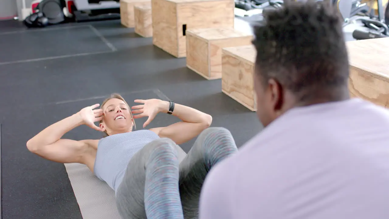 Fit young Caucasian woman exercises at the gym guided by an African American man