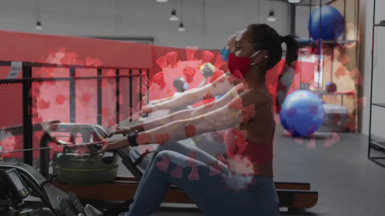 Covid 19 cells floating against two diverse woman wearing face mask working out at the gym