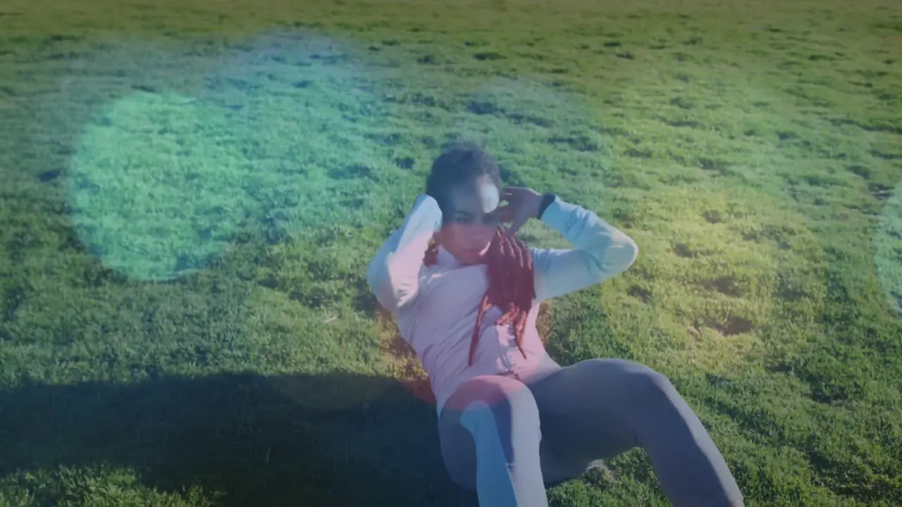 Spots of light against african american fit woman performing crunches on the grass