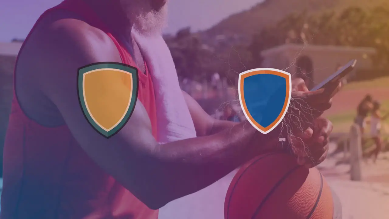 Two logo clashing against african american senior man with basketball using smartphone