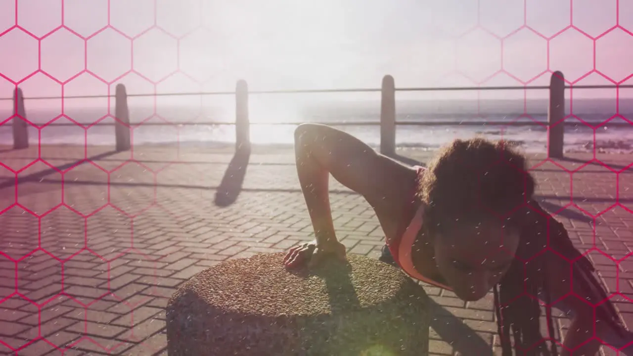 Pink hexagonal shapes against t african american fit woman performing push ups on the promenade