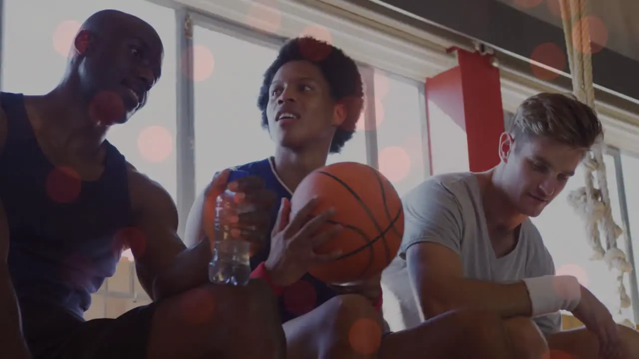 Spots of light against diverse team of male basketball players taking a break from playing in court