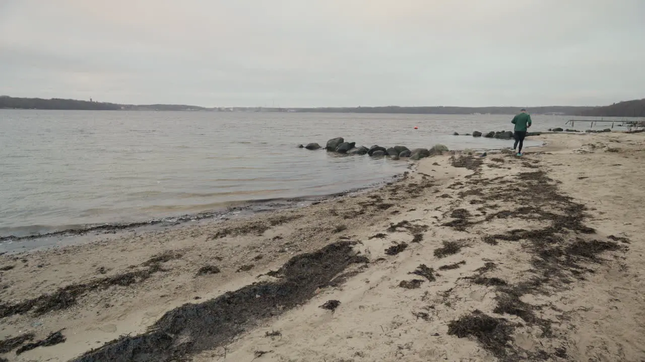 Jogger running away from the camera on a winter beach near the water on a cloudy day