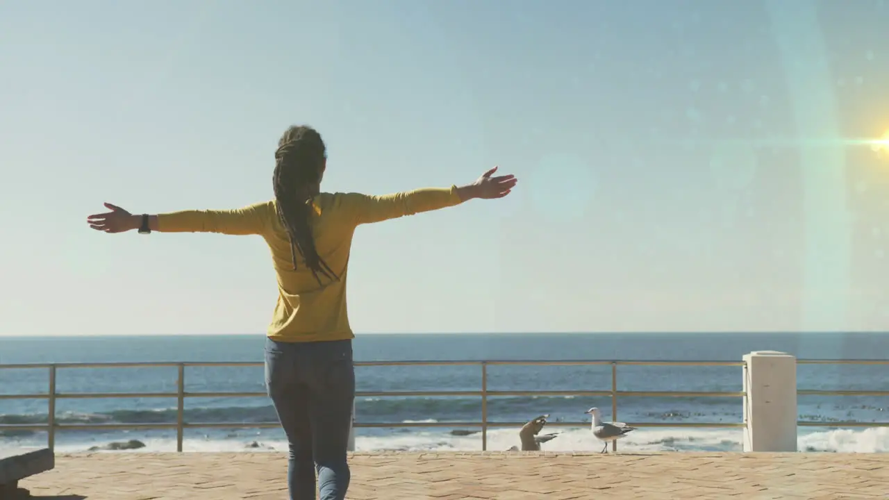 Spots of light against rear view of african american woman with her arms wide open on the promenade