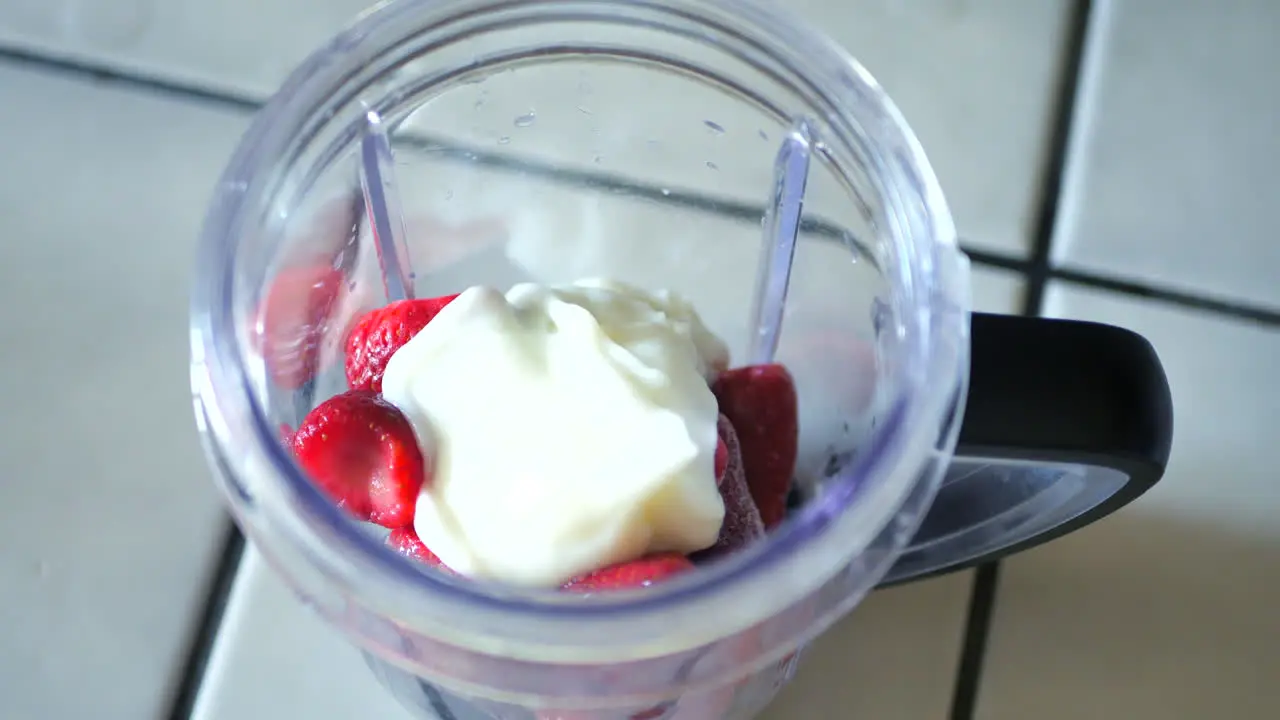 Pouring yogurt frozen blueberries and strawberries into blender to make smoothie or fitness shake