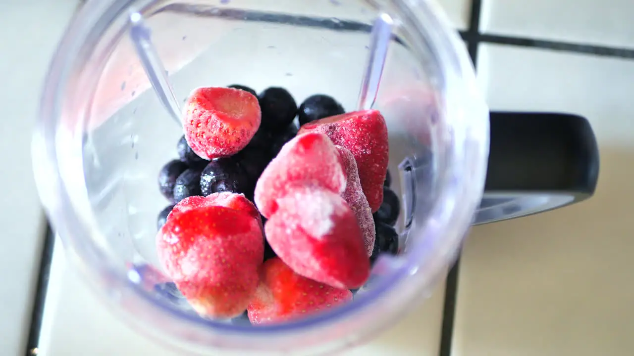 Pouring frozen blueberries and strawberries into blender to make smoothie or fitness shake