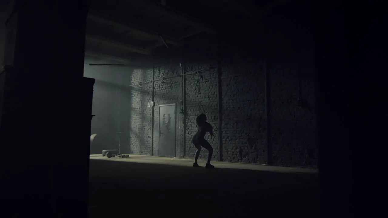 Athletic sportswoman throwing fit ball against concrete wall in loft building