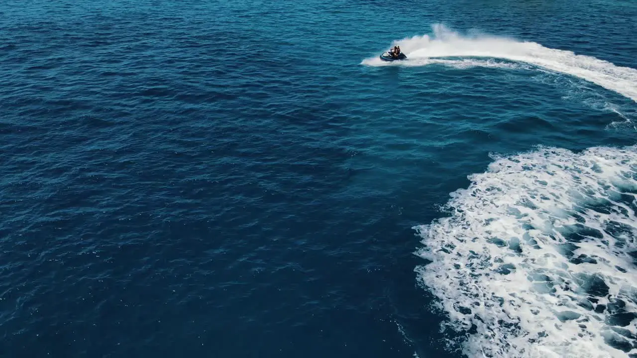 Two people are riding water scooter jet ski making circles and rotating moves on water surface attractive aerial view captured near the coastline of Ibiza Spain