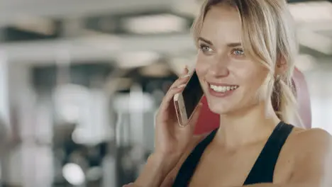 Beautiful woman talking smartphone in fitness gym Smiling girl having break