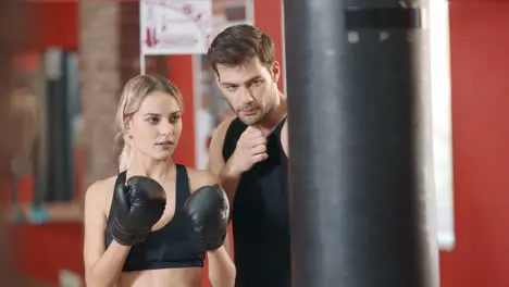 Sport woman boxing punching bag in gym club with personal trainer