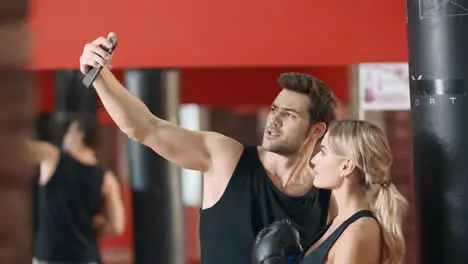 Happy couple making selfie in fitness gym Woman and man taking mobile photo