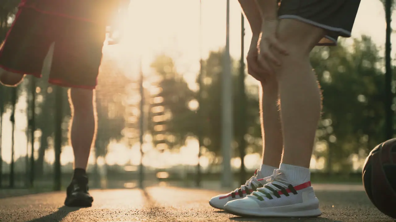 Close Up Of Two Basketball Players Stretching Their Legs In An Outdoor Baskeball Court