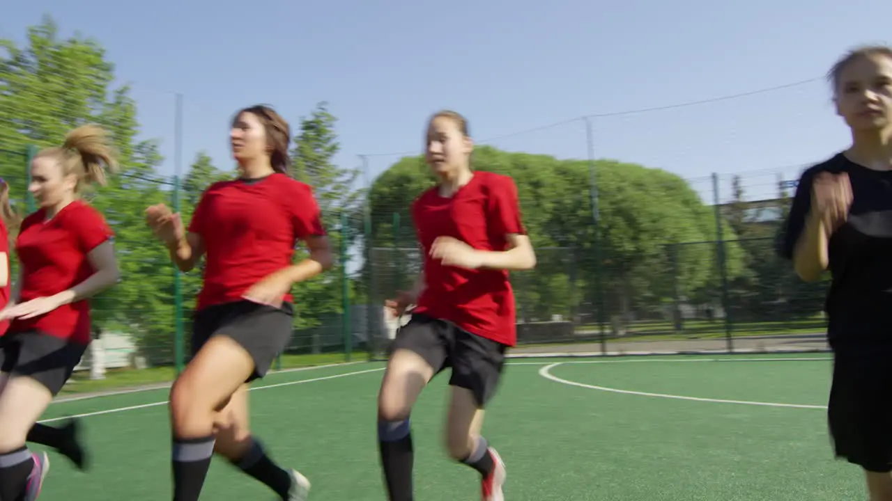 Team Of Young Female Soccer Players In Uniform Running On Field Together While Training Outdoors On Sunny Summer Day