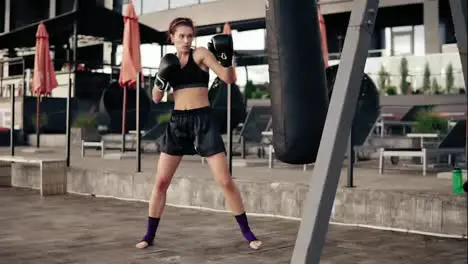 Strong athletic female boxer in gloves exercising with a bag Workout outside Female boxer training Self defence concept