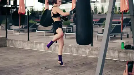 High pace video Strong athletic female boxer in gloves exercising with a bag She hits a bag with her leg Workout outside