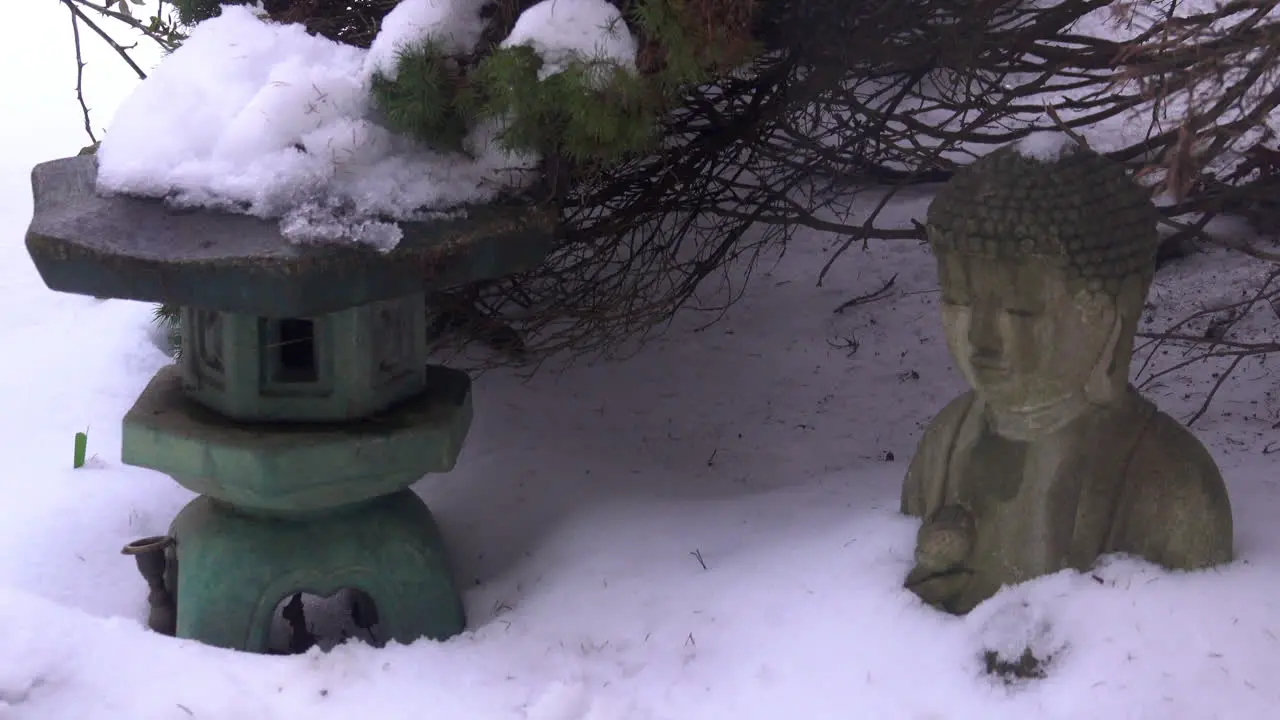 Snow slowly melts and drips piled atop a Japanese lantern and Buddha statue