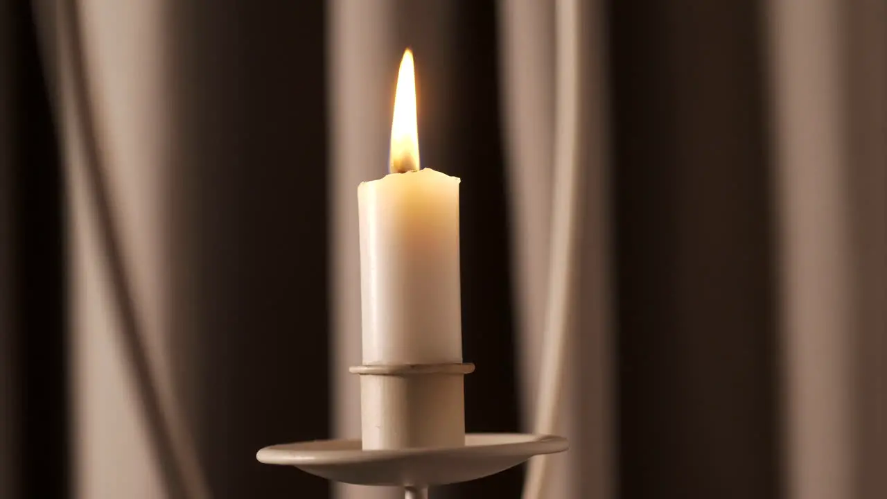 Soft candle burns in front of drapes with moving shadows close up