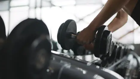 Female hands taking bodybuilding dumbbells in gym club