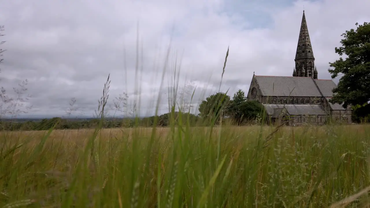 UK church and steeple through hayfield in village and tree lined