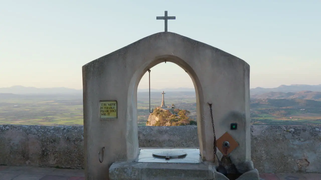 View from the Monastery of San Salvador Mallorca overlooking a hill with a cross and mountains in the background