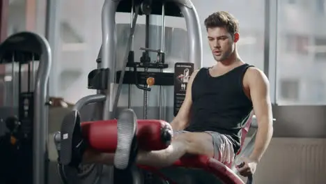 Strong sportsman doing legs exercise on sport simulator in fitness club