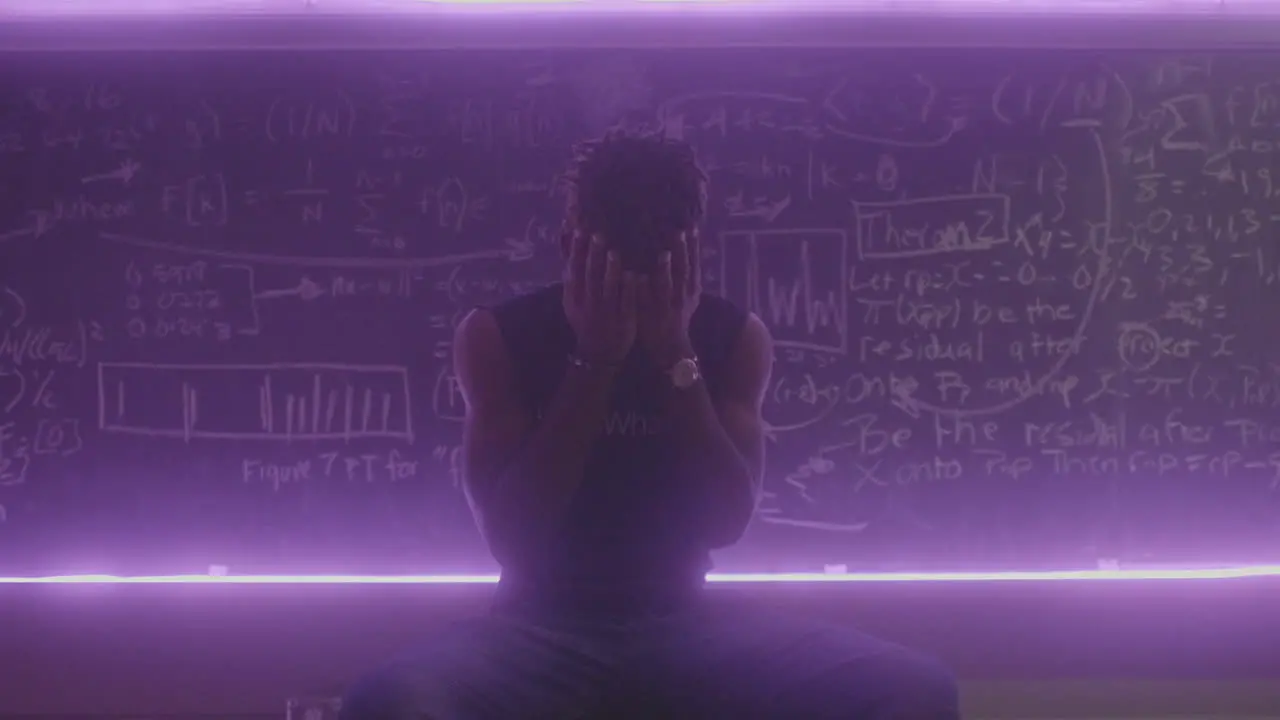 African American male sitting on a stool in front of a chalkboard with extreme frustration