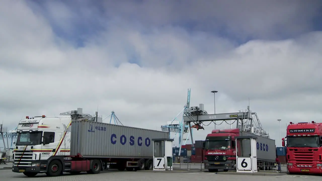 Trucks with COSCO shipping containers at a port terminal with gantry cranes in the background