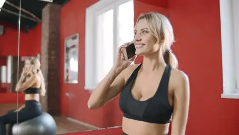 Fitness woman calling mobile phone in gym club Young woman sitting on gym ball