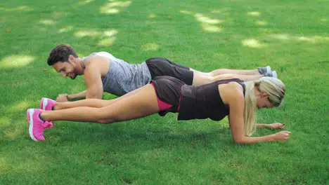 Fitness couple man and woman training plank exercise on grass in summer park