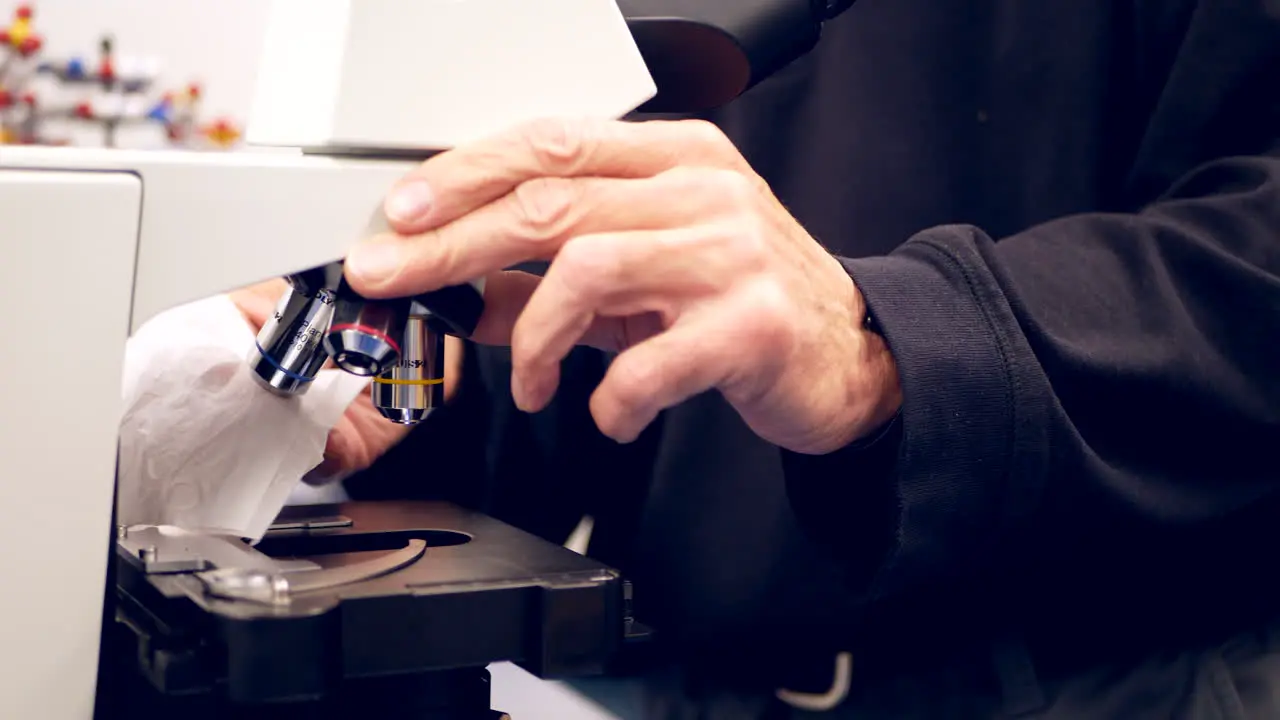 A college professor cleaning the lens of a microscope to show his students in a biology research laboratory