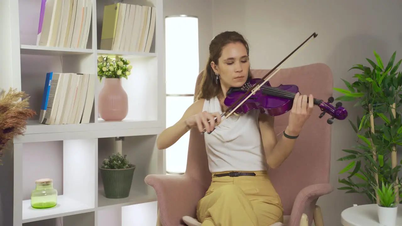 Talented musician woman playing violin sitting on sofa at home