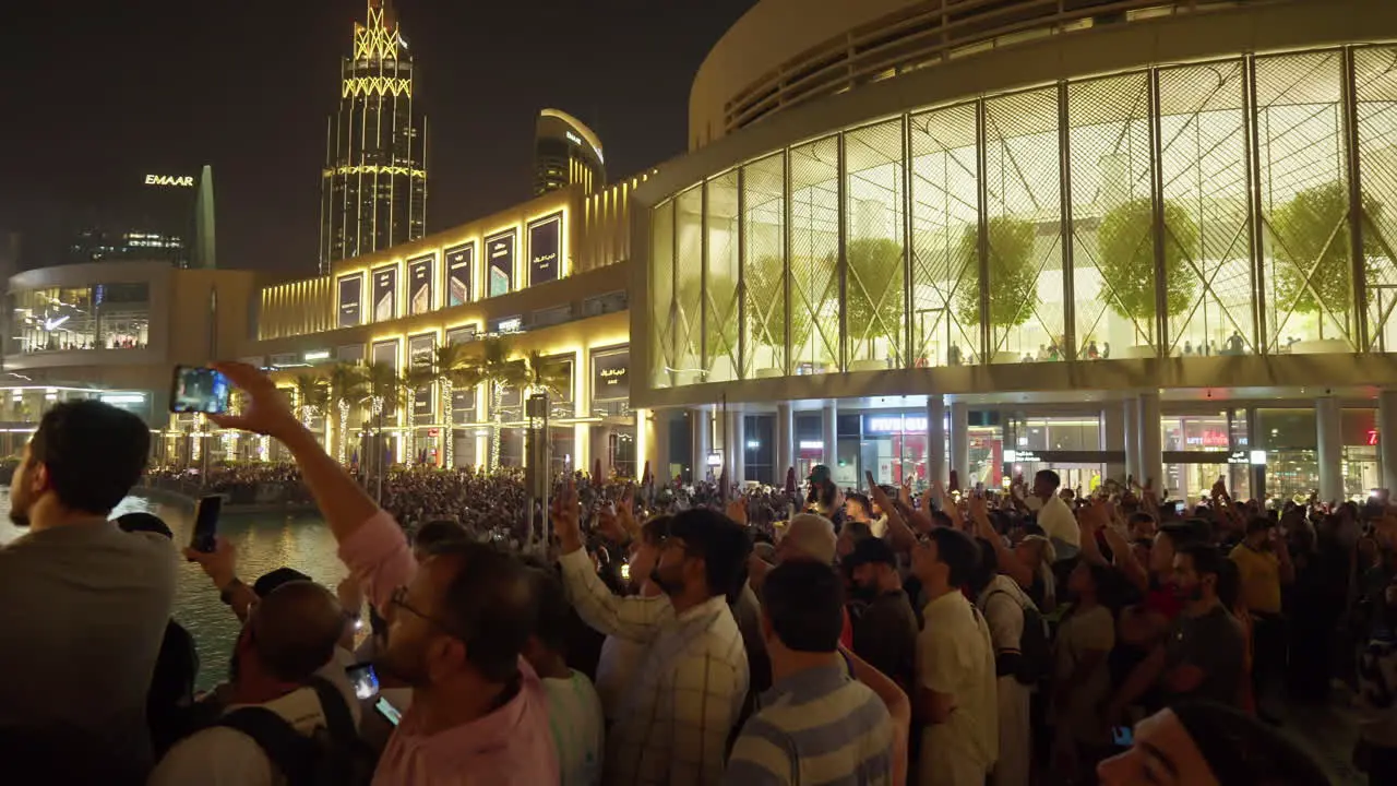 Crowded plaza with people filming a nighttime event in Dubai