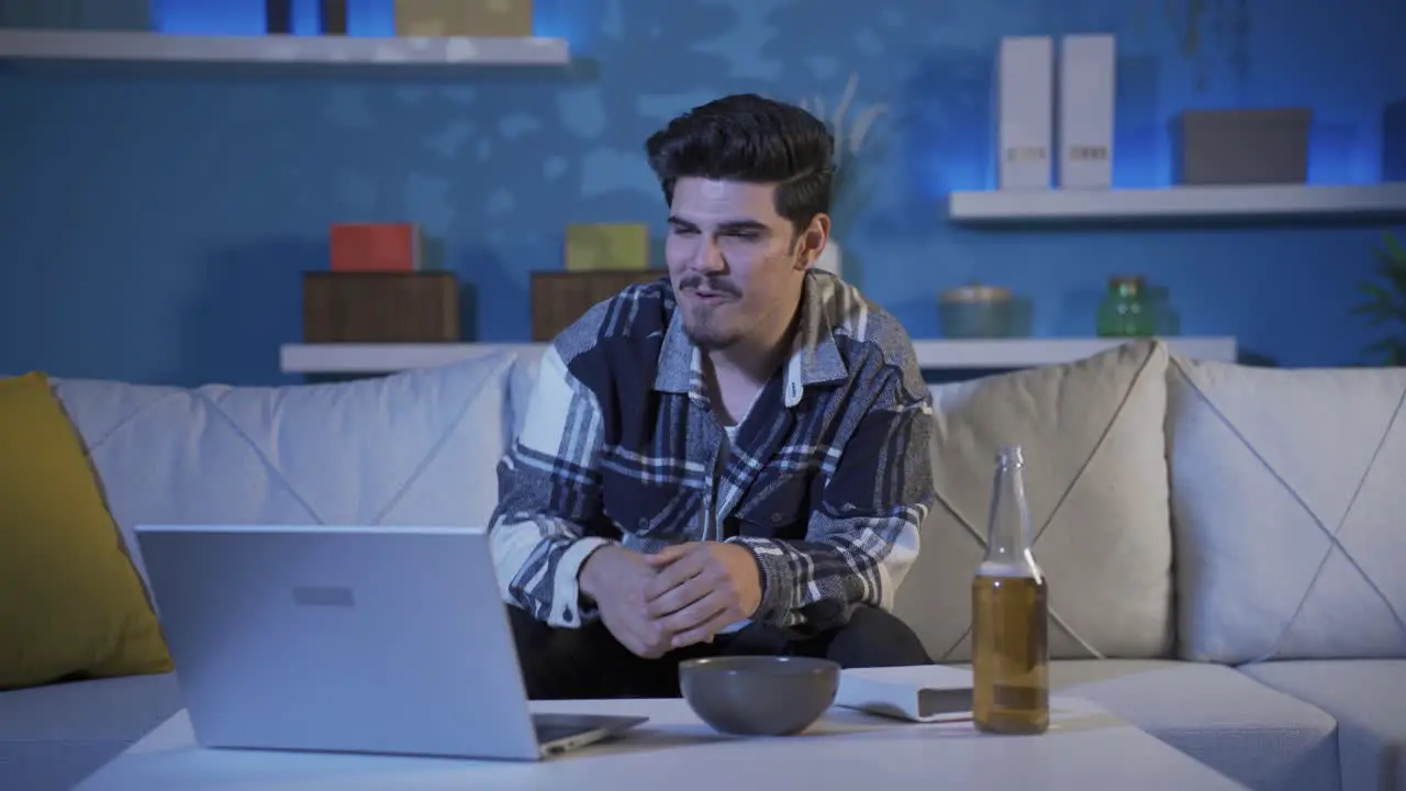 Young man watching movie at night on laptop at home He is drinking alcohol