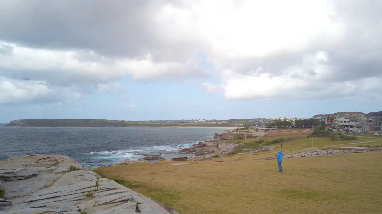 Man in blue is playing with a model remote control aircraft near a beach in a windy cloudy day