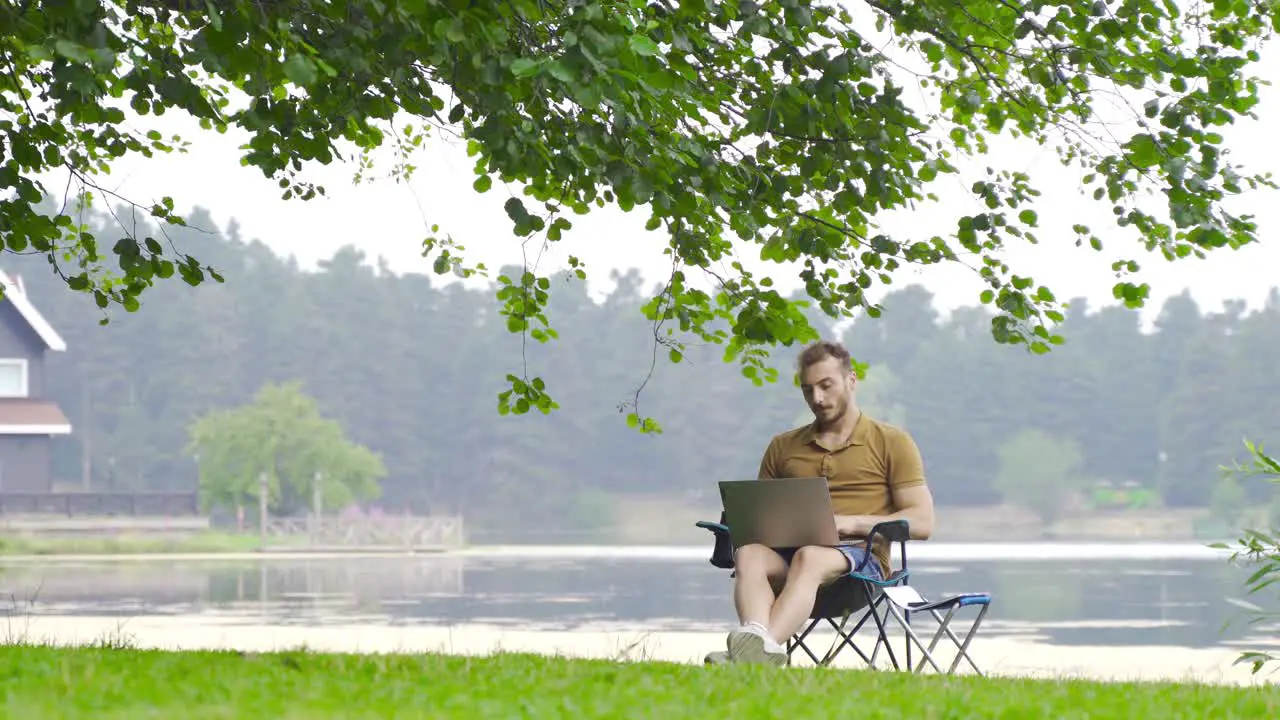 Man working with computer by lake in nature